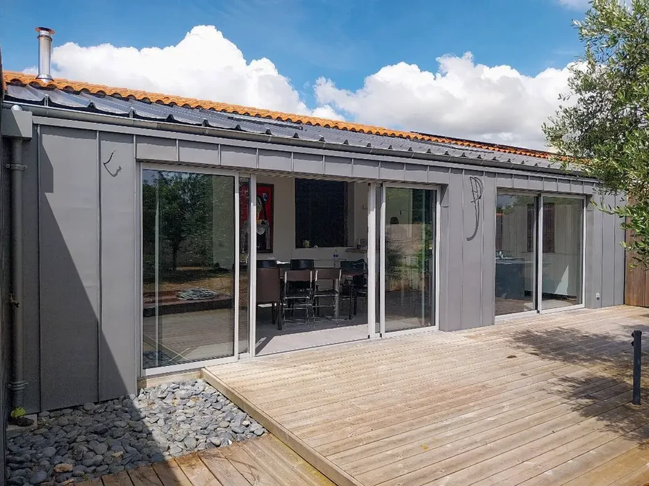 Véranda moderne avec structure aluminium gris anthracite, toiture tuiles mécaniques oranges et panneaux photovoltaïques