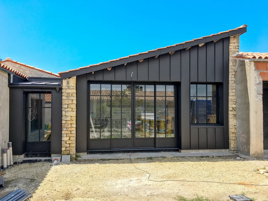Chantier de construction résidentielle en cours avec bâtiment moderne à bardage métallique anthracite et maçonnerie en pierre naturelle