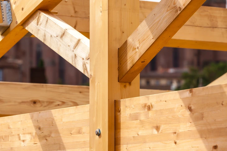 Intérieur d'un bâtiment en construction montrant la charpente en bois brut avec poutres principales et secondaires