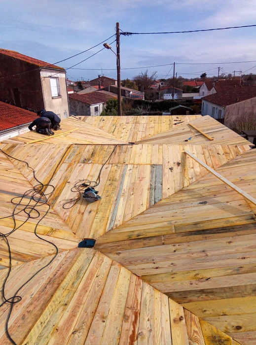 Chantier de construction extérieur avec ouvrier sur nacelle élévatrice jaune installant une structure de toiture